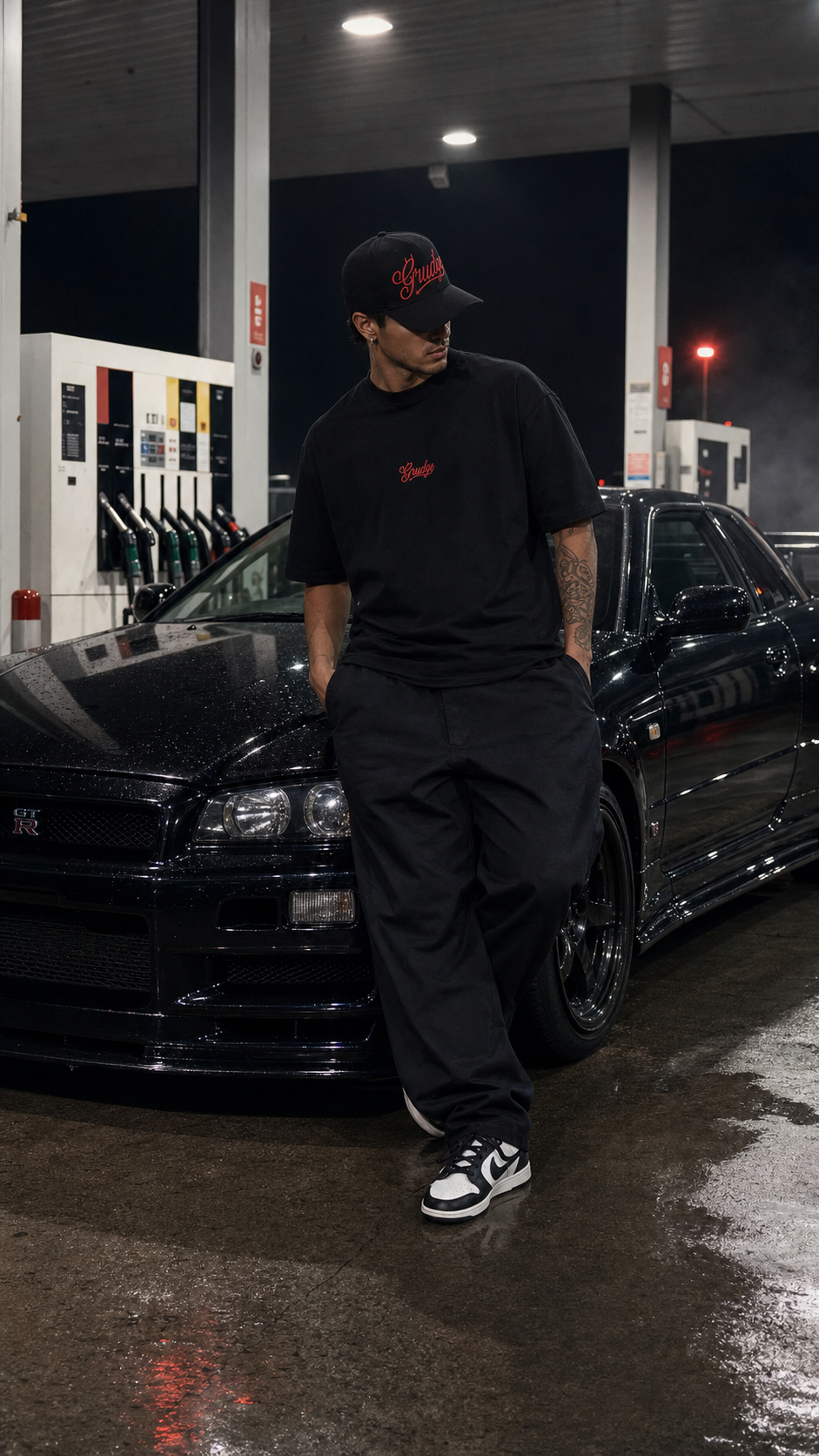 Model wearing the black Grudge tee and cap at a petrol station