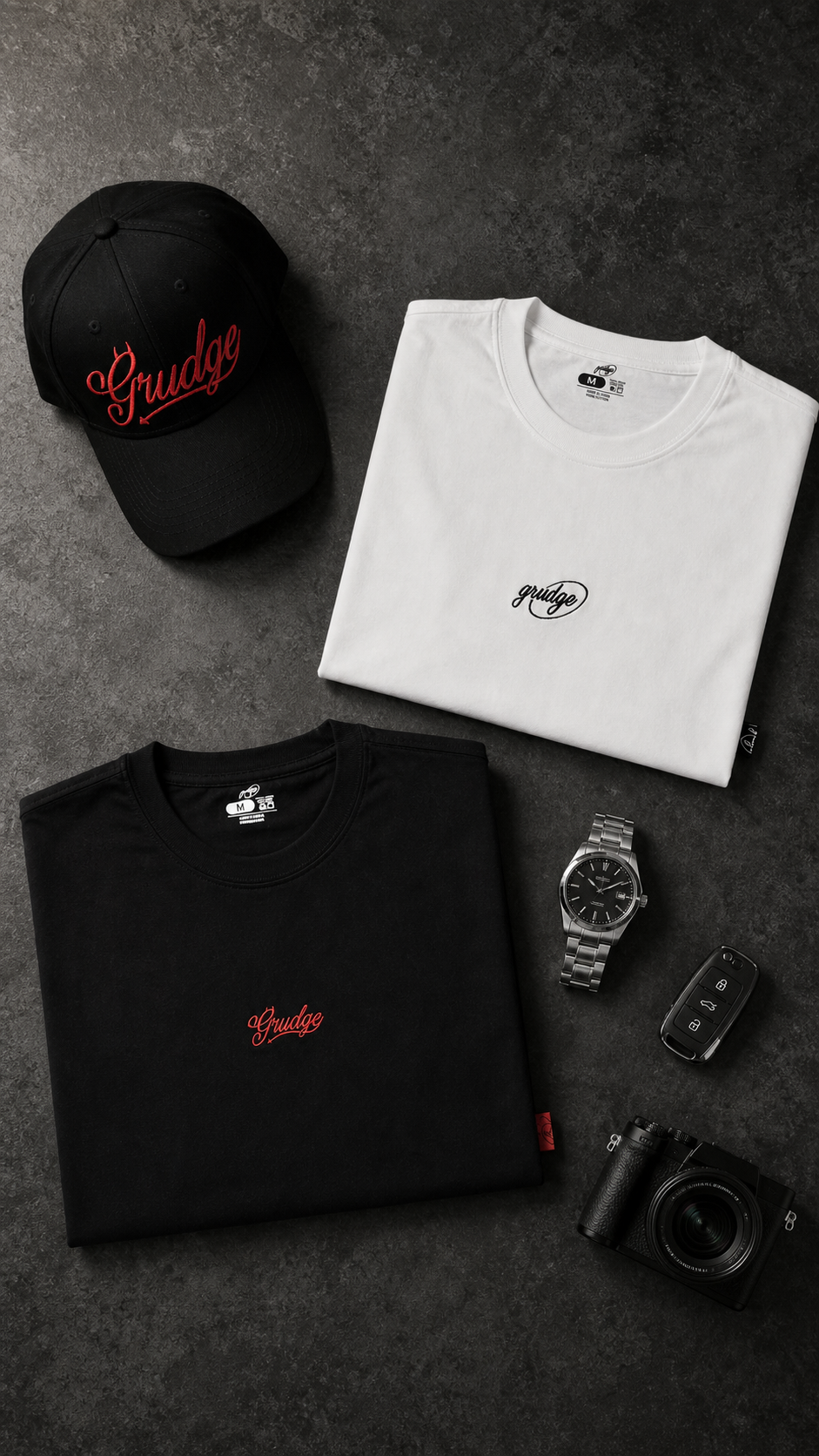 Black and white Grudge tees and cap arranged on dark concrete