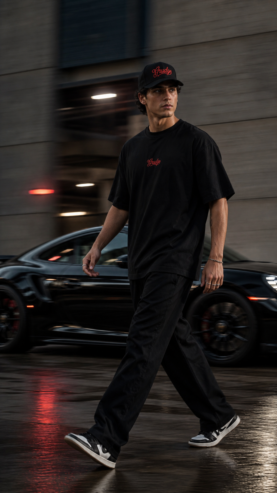 Model walking past a black sports car in the black Grudge tee and cap